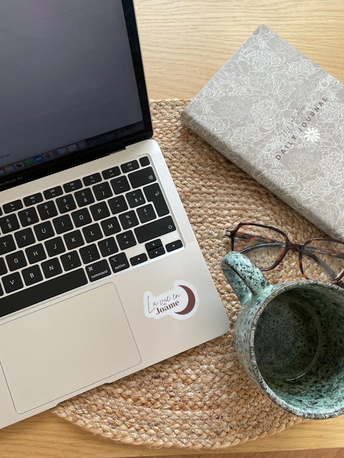 Warm home office setup with a laptop, journal, glasses, and coffee mug on a woven mat.